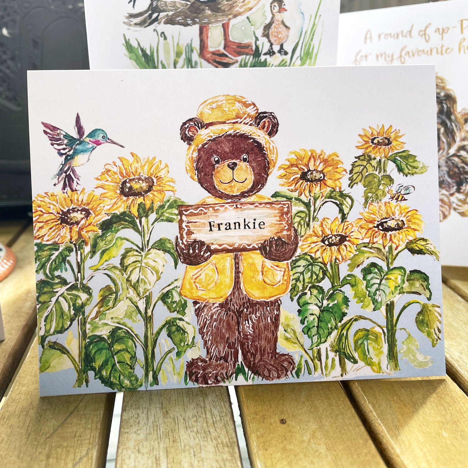 Little brown bear pokes his head in between lush trees to check in with a butterfly. it says "Just wanted to poke my head in and say hi butterfly"